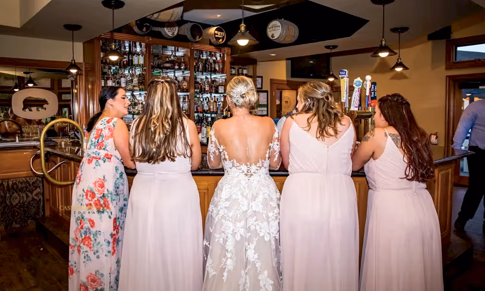 Bride and bridesmaids stand at Bear Den Grille bar during Black Bear cocktail hour.